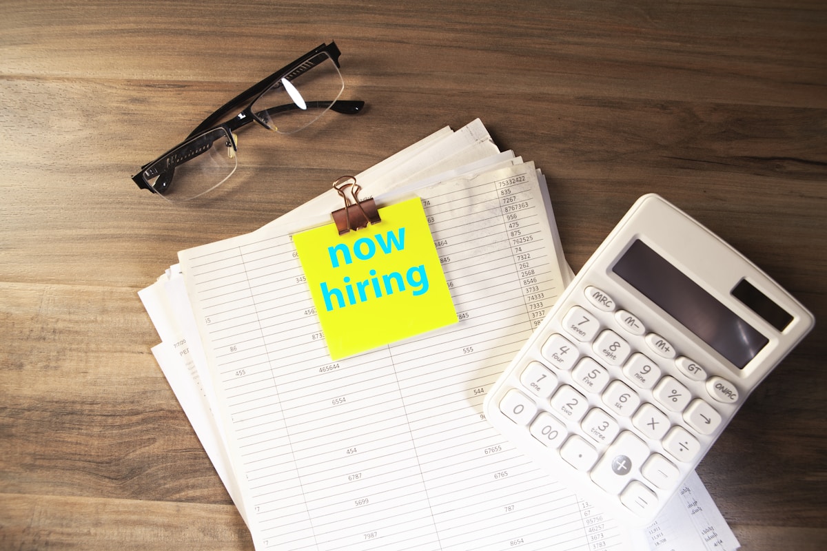 Calculator, glasses, and papers with 'now hiring' note.